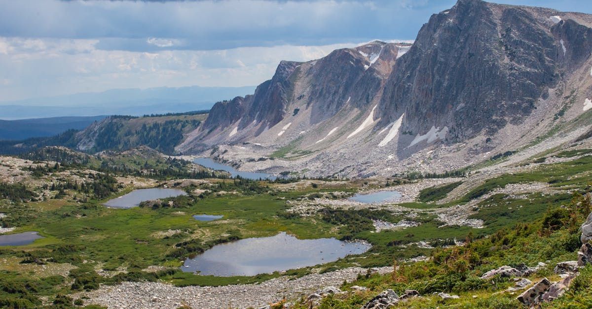 Mountain valley with alpine lakes, green meadows, and a steep rocky cliff under a blue sky