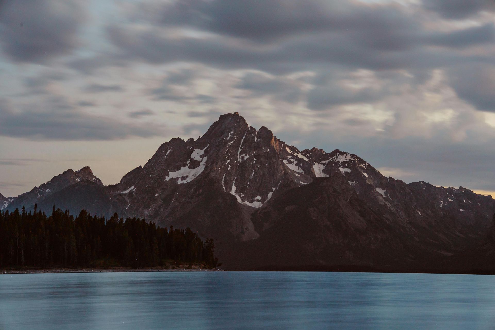 Mountain reflected in a calm lake under a cloudy sky, with a dark forest along the shore