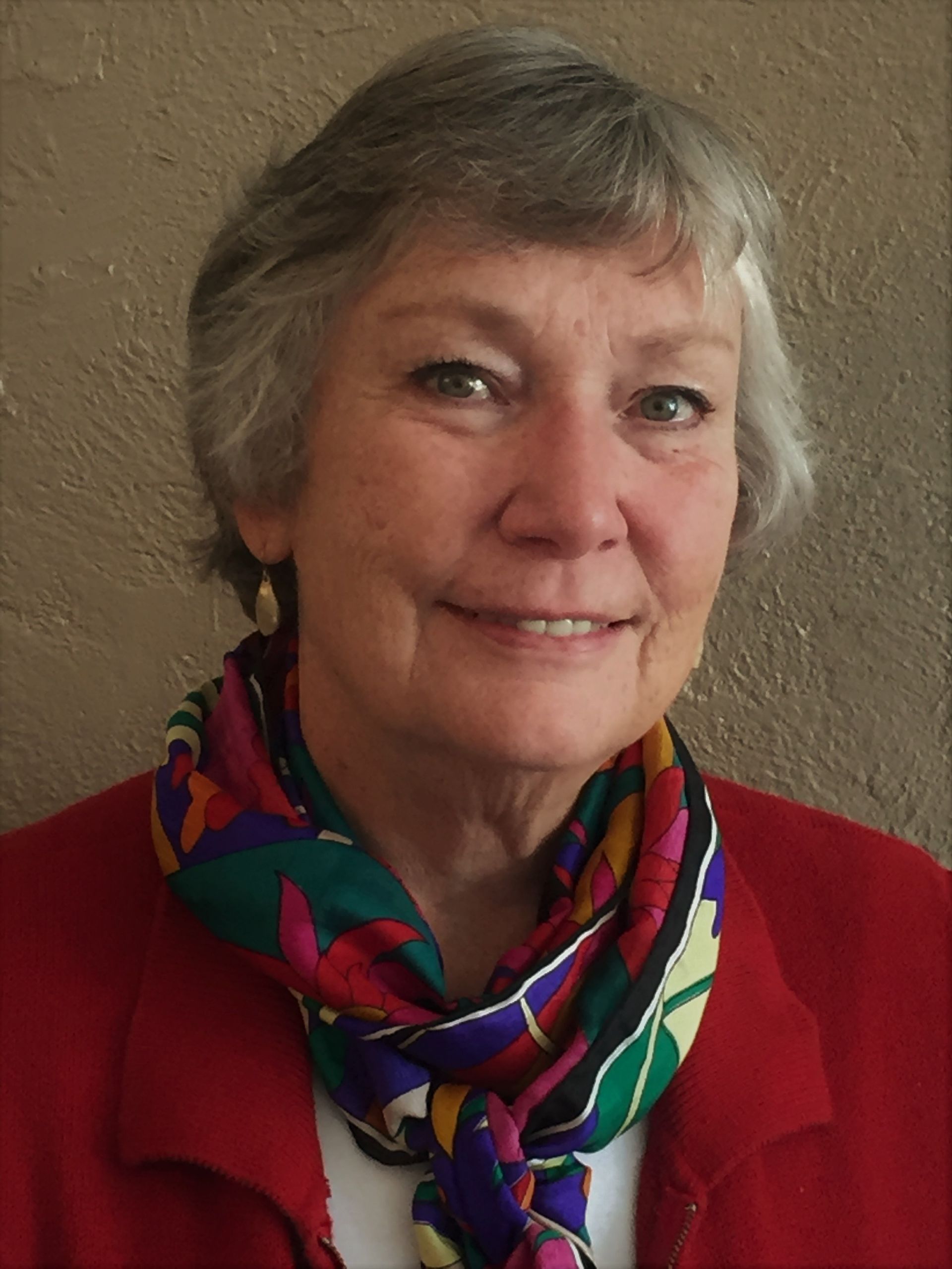 Portrait of a smiling person wearing a red jacket and colorful scarf against a plain background