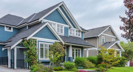 A blue and white house with a gray roof is sitting on top of a lush green lawn.