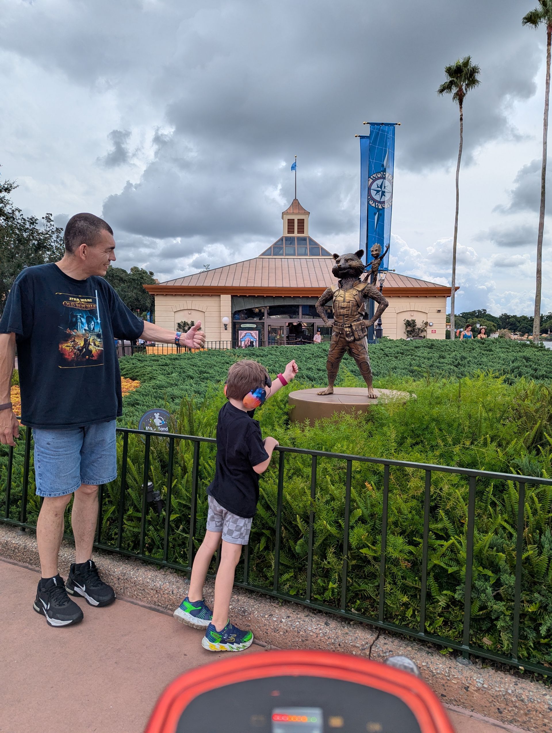 Man and child looking at a golden statue of a girl in front of green bushes.