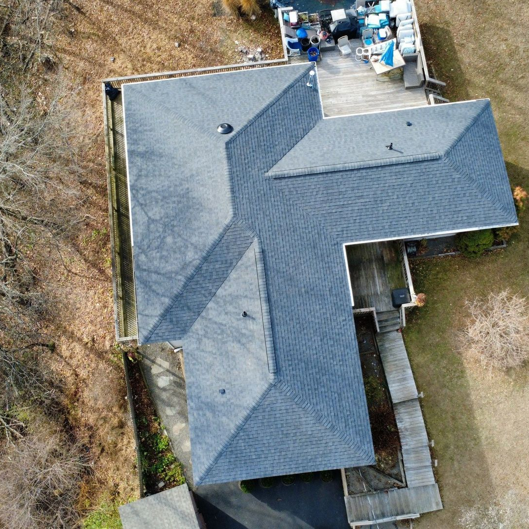 Aerial view of a house under construction with a gray shingle roof and green sheathing. Aerial view of a house under construction with a gray shingle roof and green sheathing.