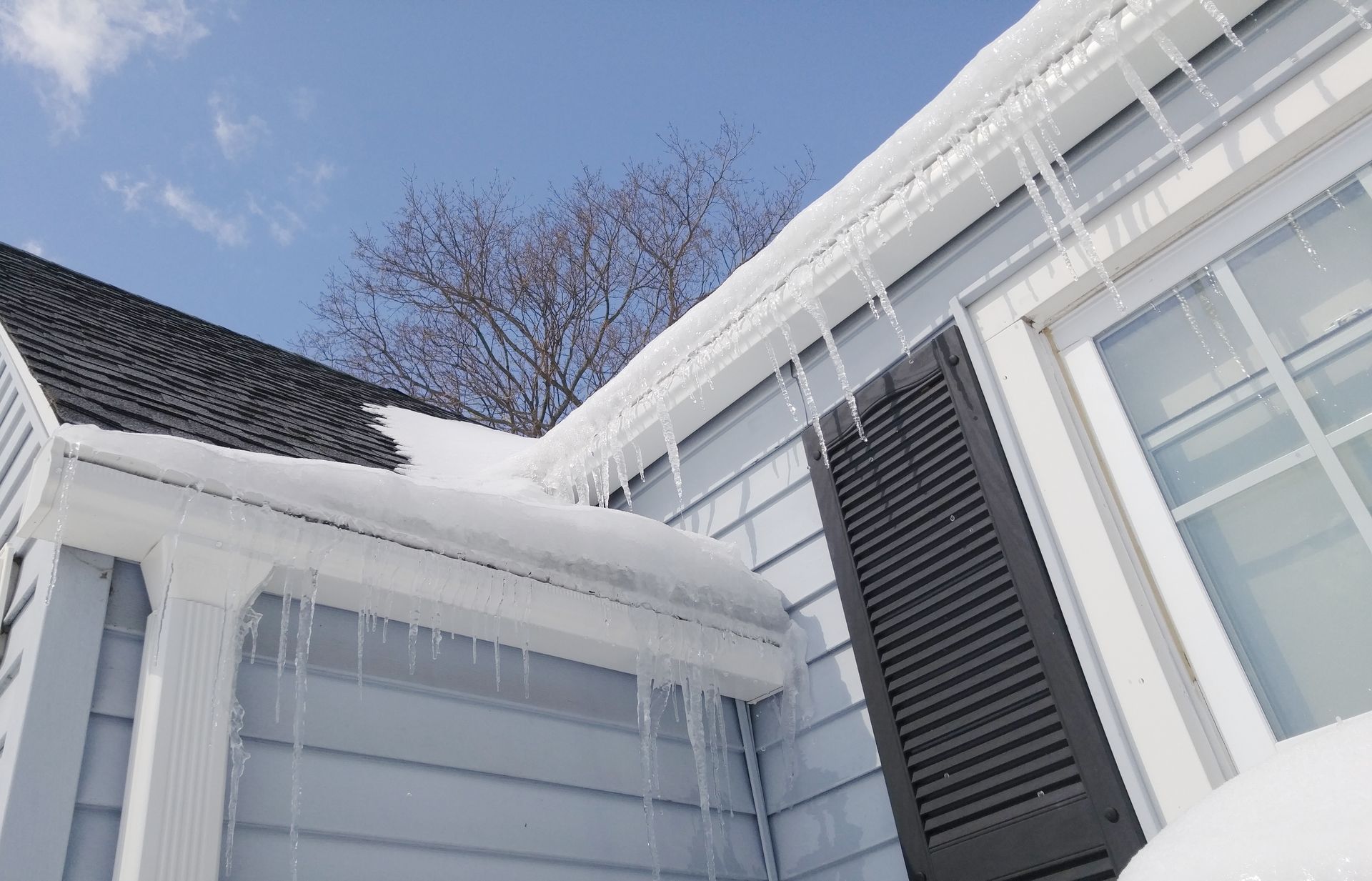Snow-covered roof with icicles hanging from the gutters on a house with a blue sky background.
