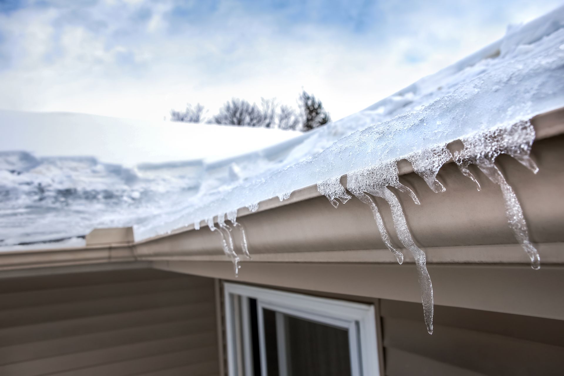 Ice dam buildup along the edge of a snow-covered asphalt shingle roof with icicles hanging from the 