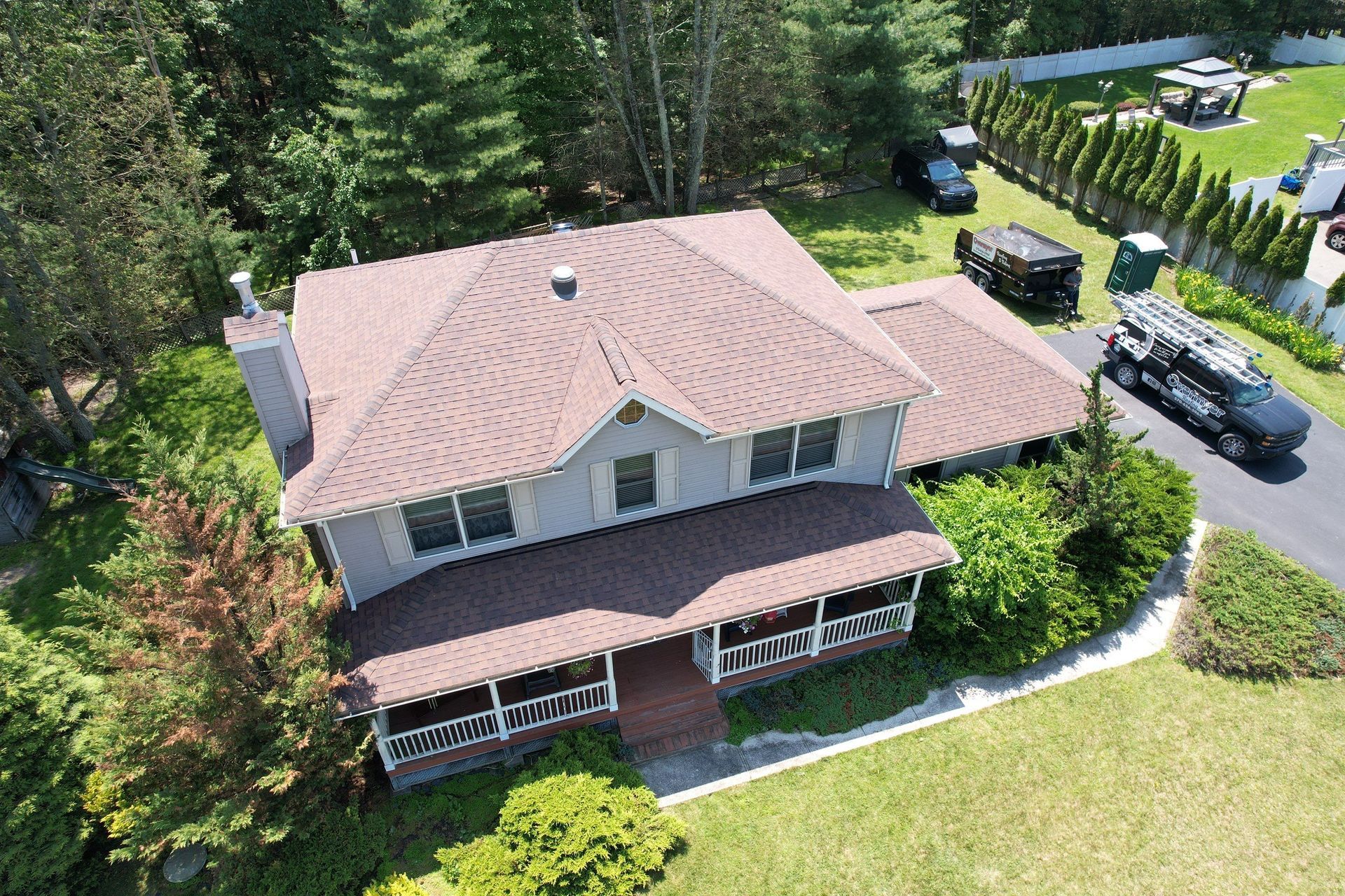 Aerial view of a gray house with a brown roof and porch, surrounded by trees and green grass.
