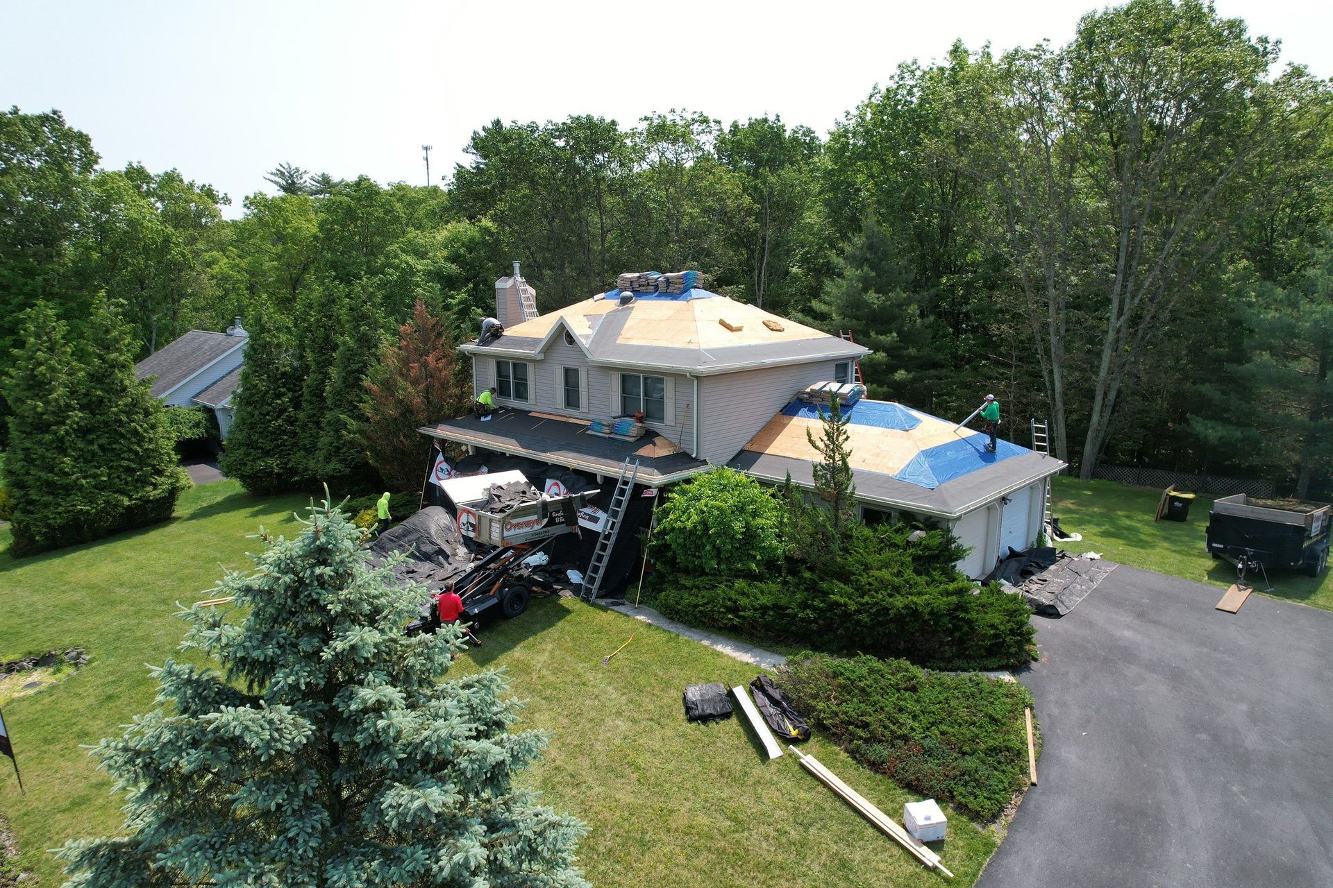 House with roof being replaced on a sunny day; trees surround the home.