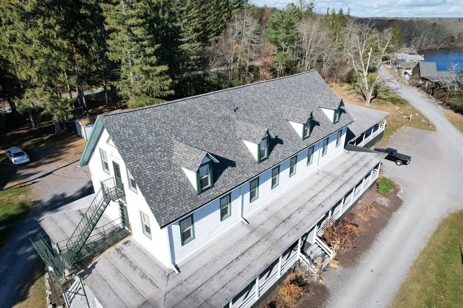 White building with gray roof, green trim, and dormer windows, near a road and water.