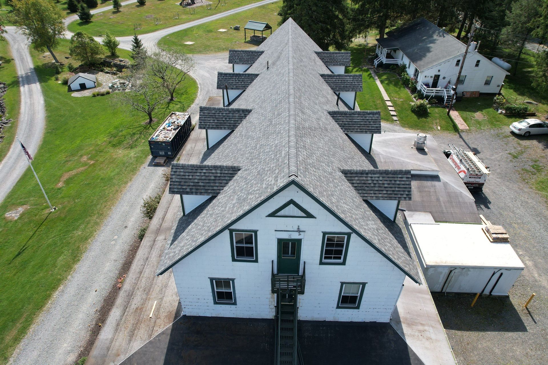 Aerial view of a white, multi-gabled building with a green door and trim, set on a green grassy property.