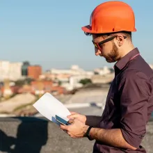 A man wearing an orange hard hat is looking at a piece of paper