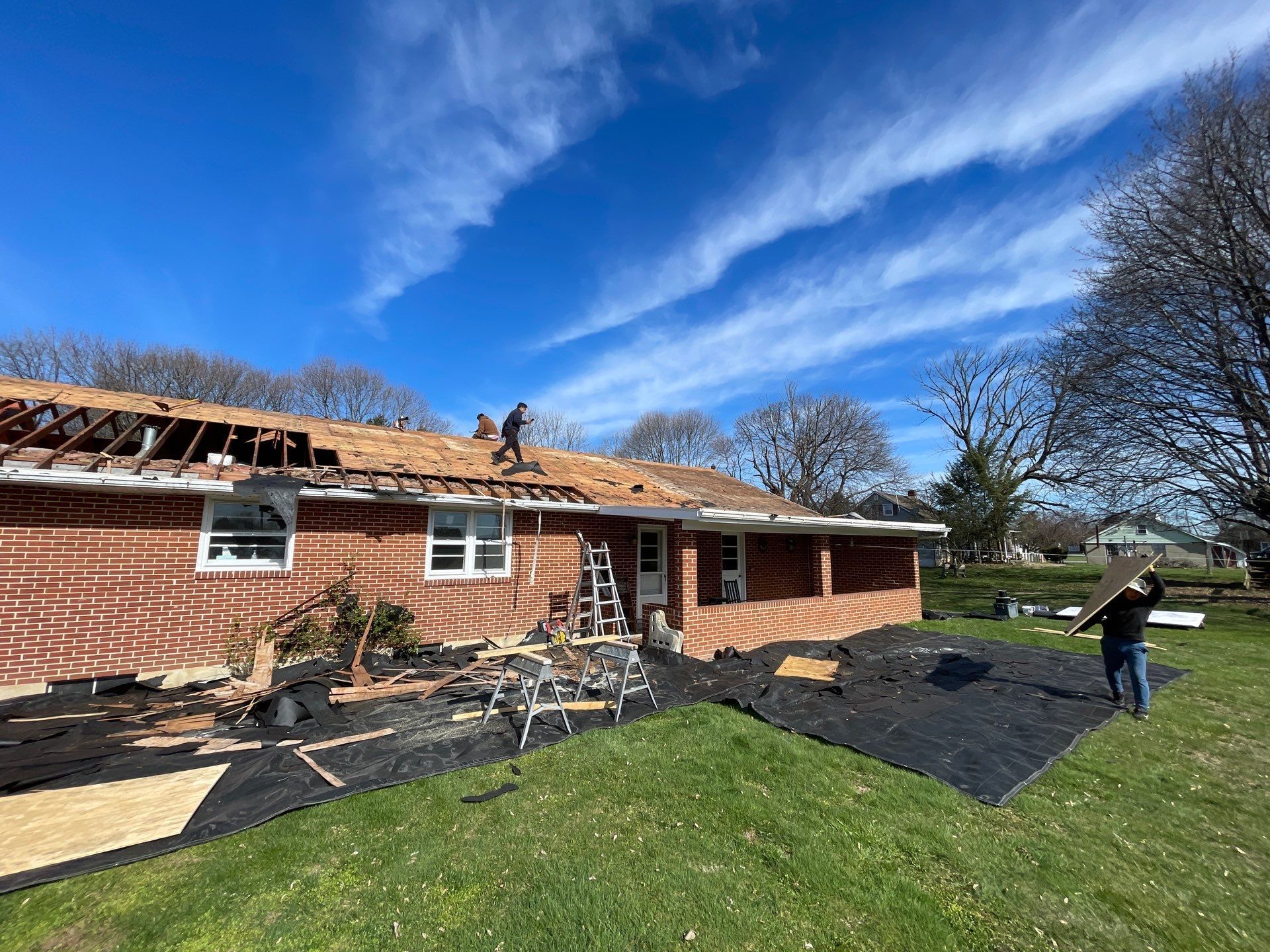Roofers removing shingles from a brick house under a blue sky.