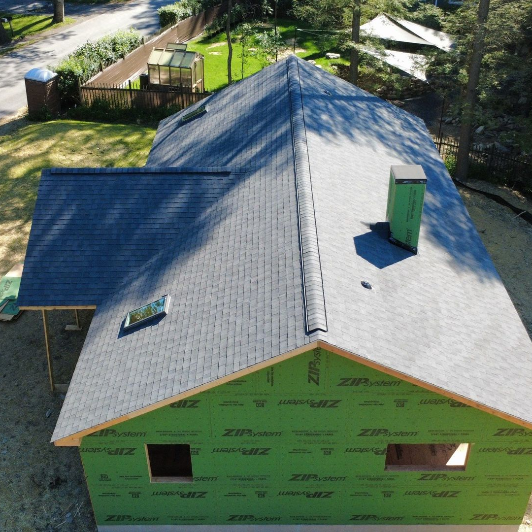 Aerial view of a house under construction with a gray shingle roof and green sheathing. Aerial view of a house under construction with a gray shingle roof and green sheathing.
