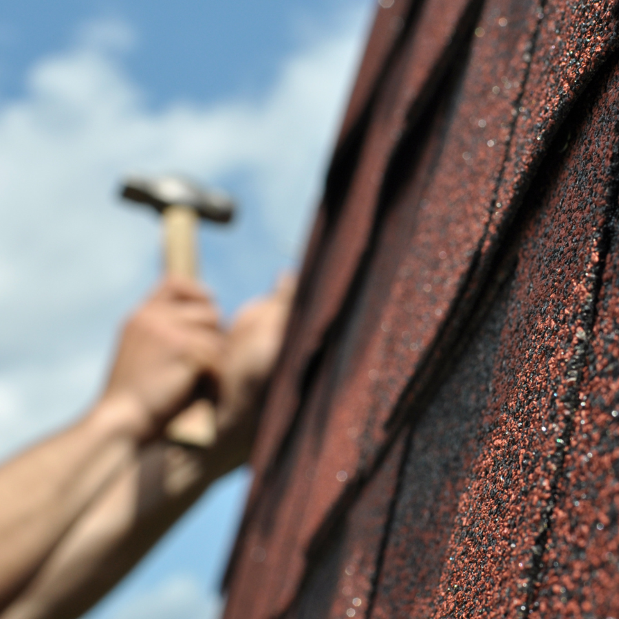 A person is holding a hammer in front of a roof