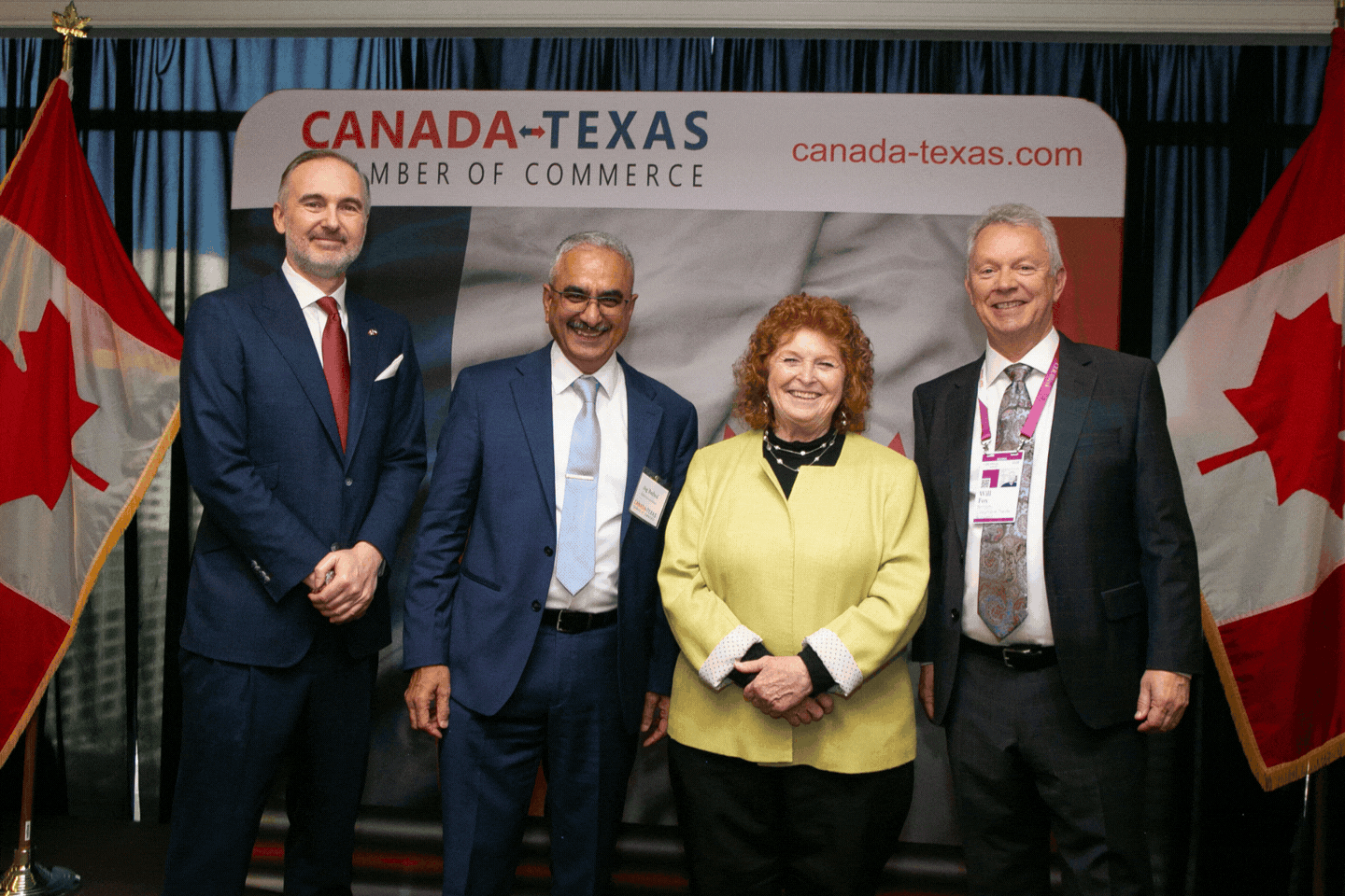 Four people standing in front of a Canada-Texas Chamber of Commerce sign flanked by two Canadian flags.