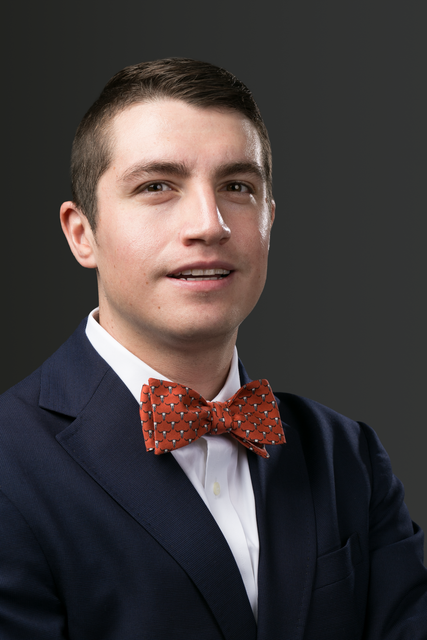 A man in a blue suit and white shirt is standing in a dark room.