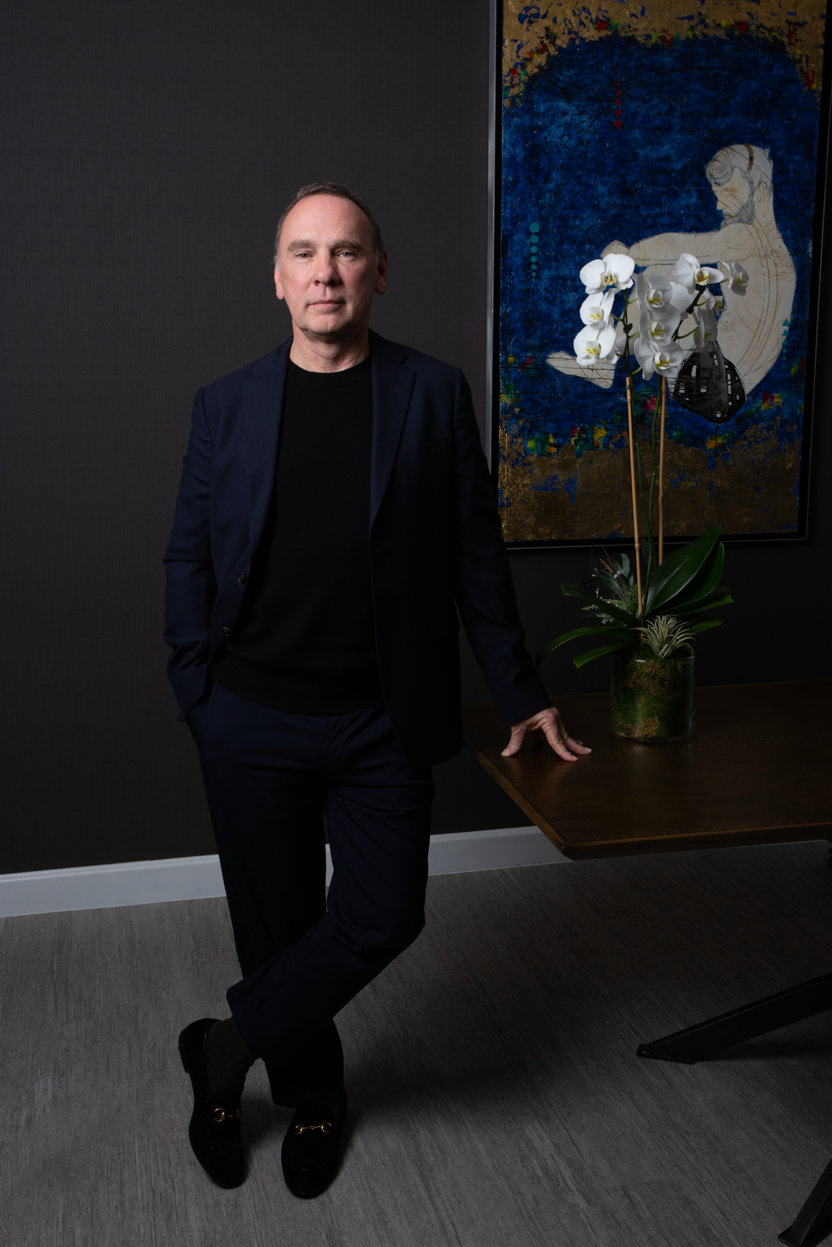 A man in a suit is standing next to a table in front of a painting.