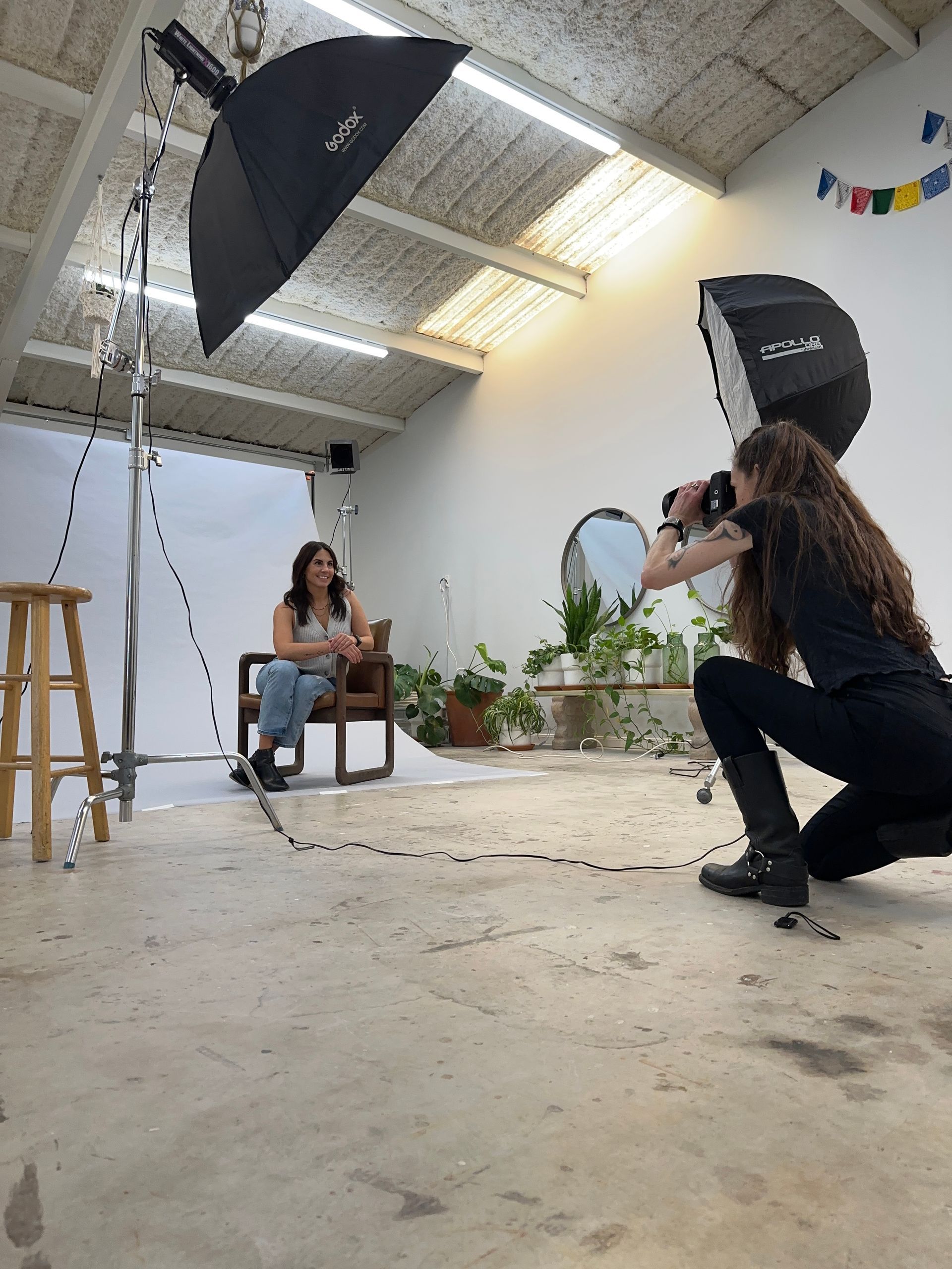 Photo shoot in a bright studio with a seated subject and photographer using large softbox lights.