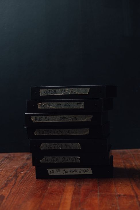 Stack of black negative binders on a wooden table against a dark background. Film photography books of negatives.