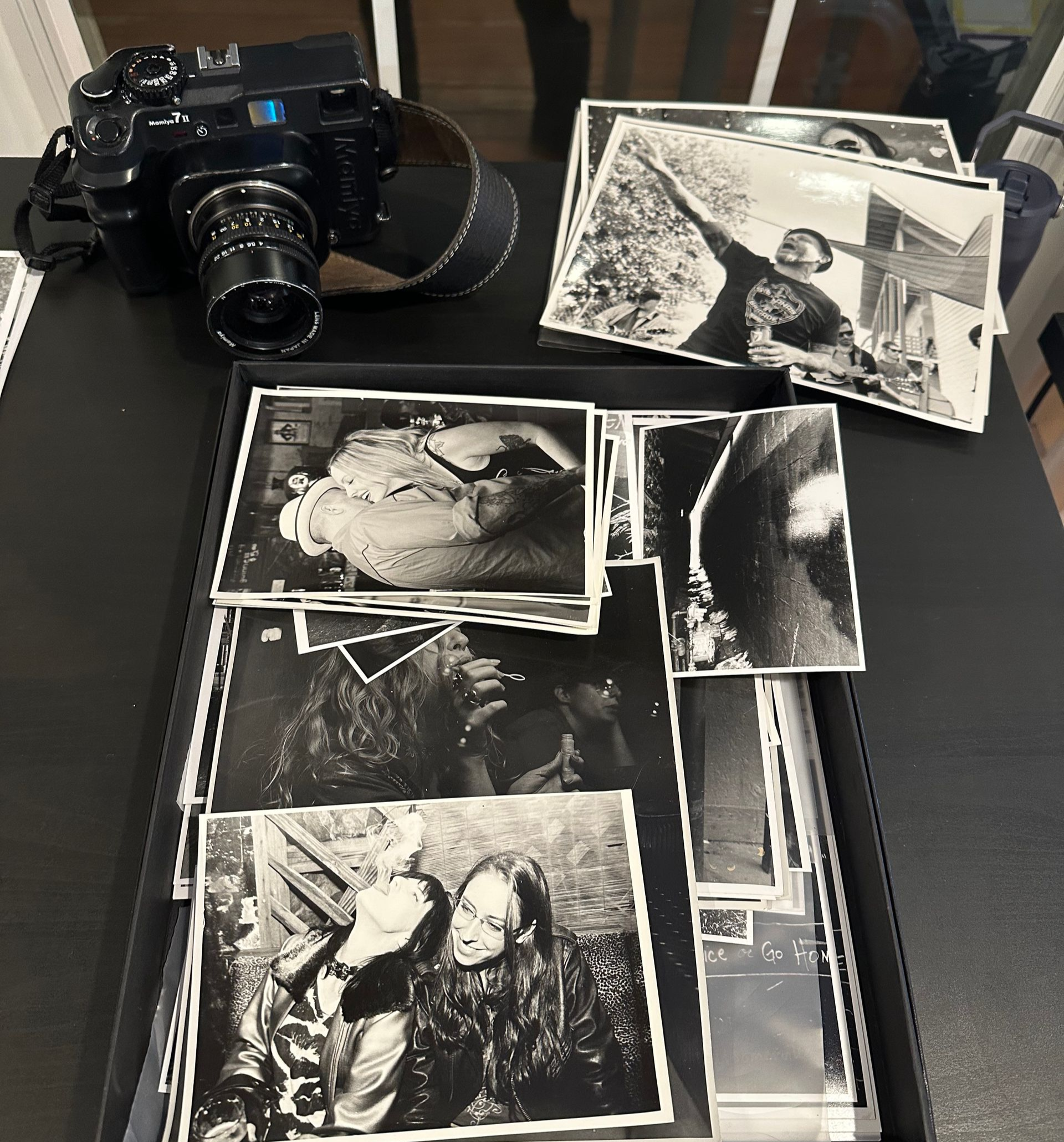 Black camera beside a stack of black-and-white printed photos on a dark table