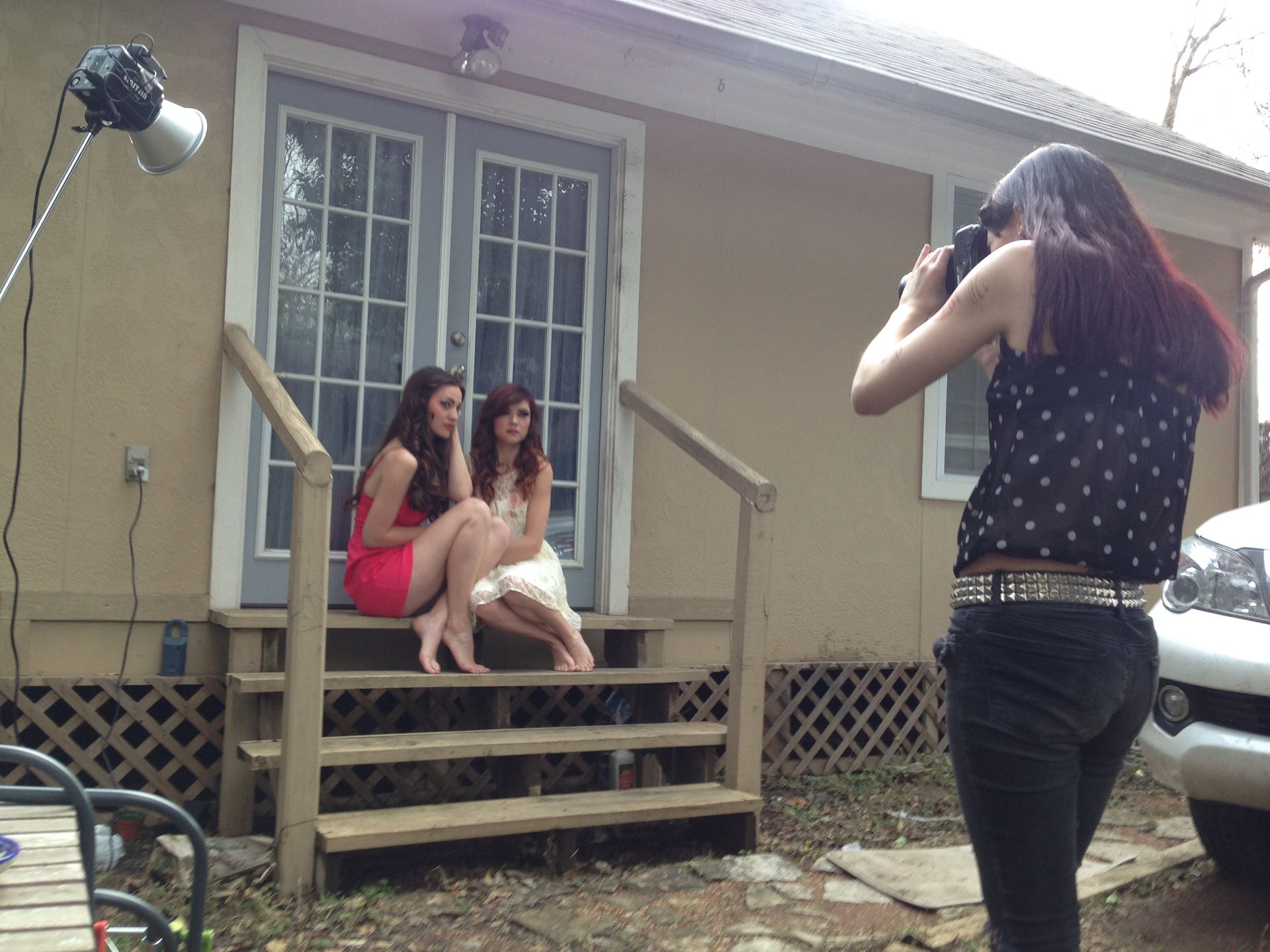 Two women sit on porch steps while another takes their photo outside a small house
