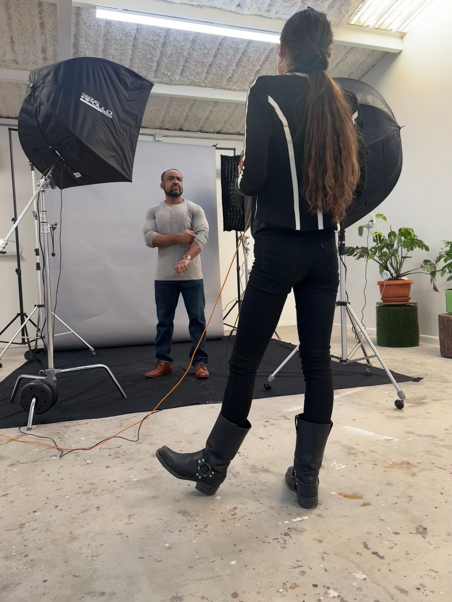 Photo shoot in a studio with two people, lighting stands, and large black softboxes.