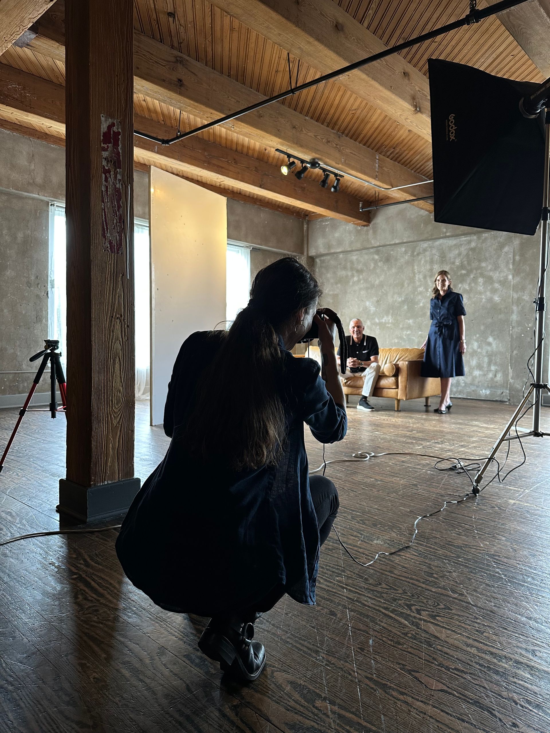 Photographer in a loft studio aims camera at a model near a large light panel during a photo shoot