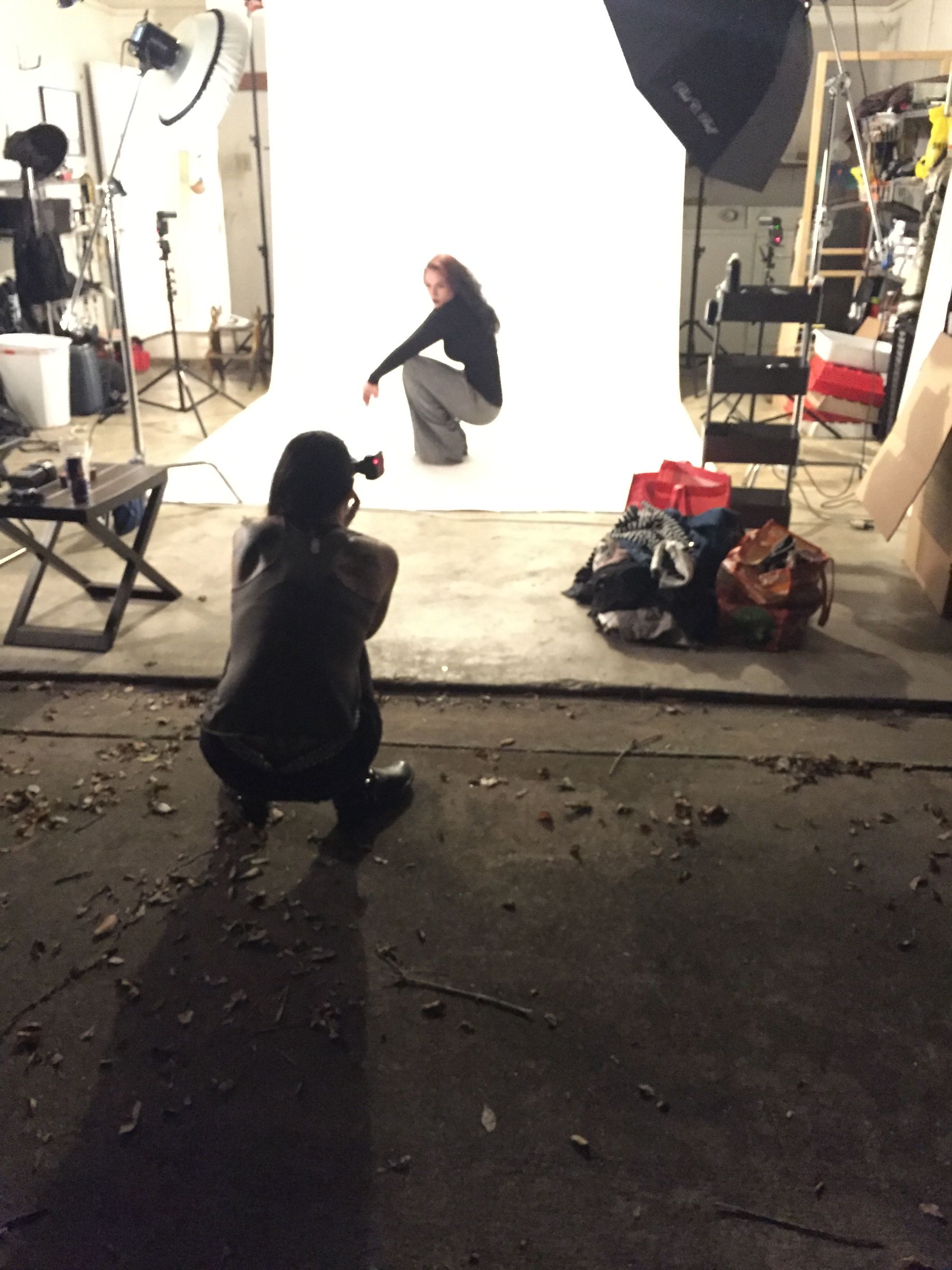 Person crouches for a photo in a studio with white backdrop and lighting equipment.