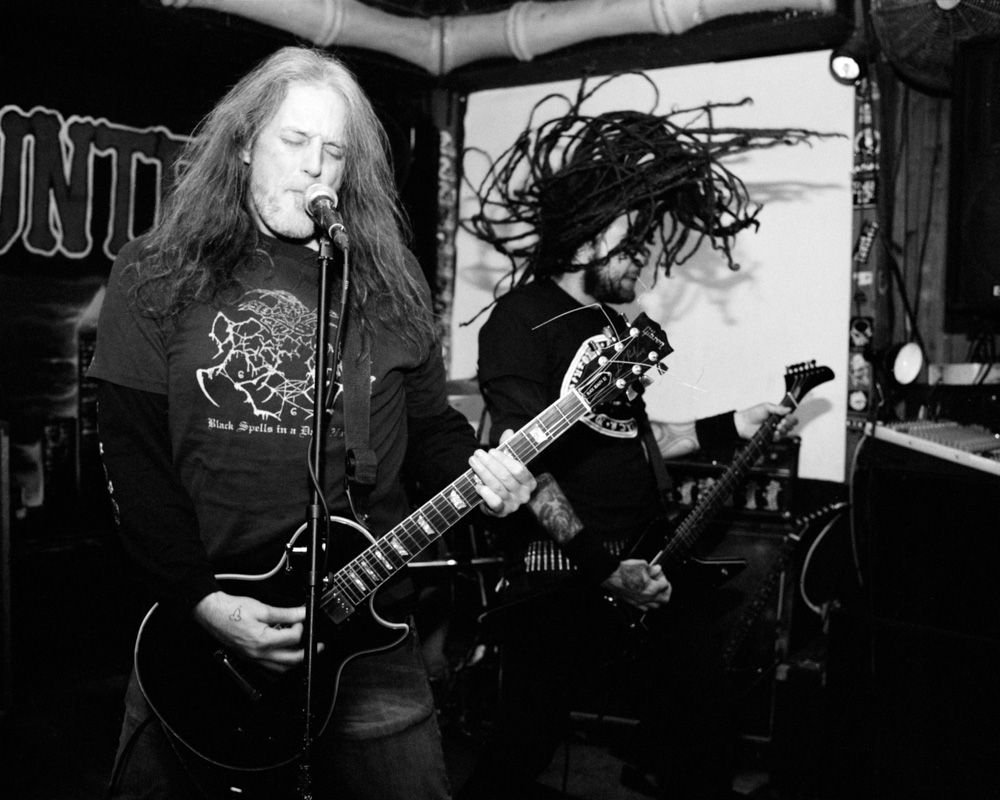 Black-and-white photo of a long-haired heavy metal guitarist performing onstage with another musician behind him. Shot on medium format film by Madison Avery Somerville. Developed and printed in a traditional wet darkroom by the photographer.