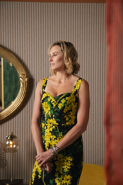 Brand photograph of a woman in a black-and-yellow floral dress standing beside a round mirror in a striped room at Sesh Coworking in Houston, TX