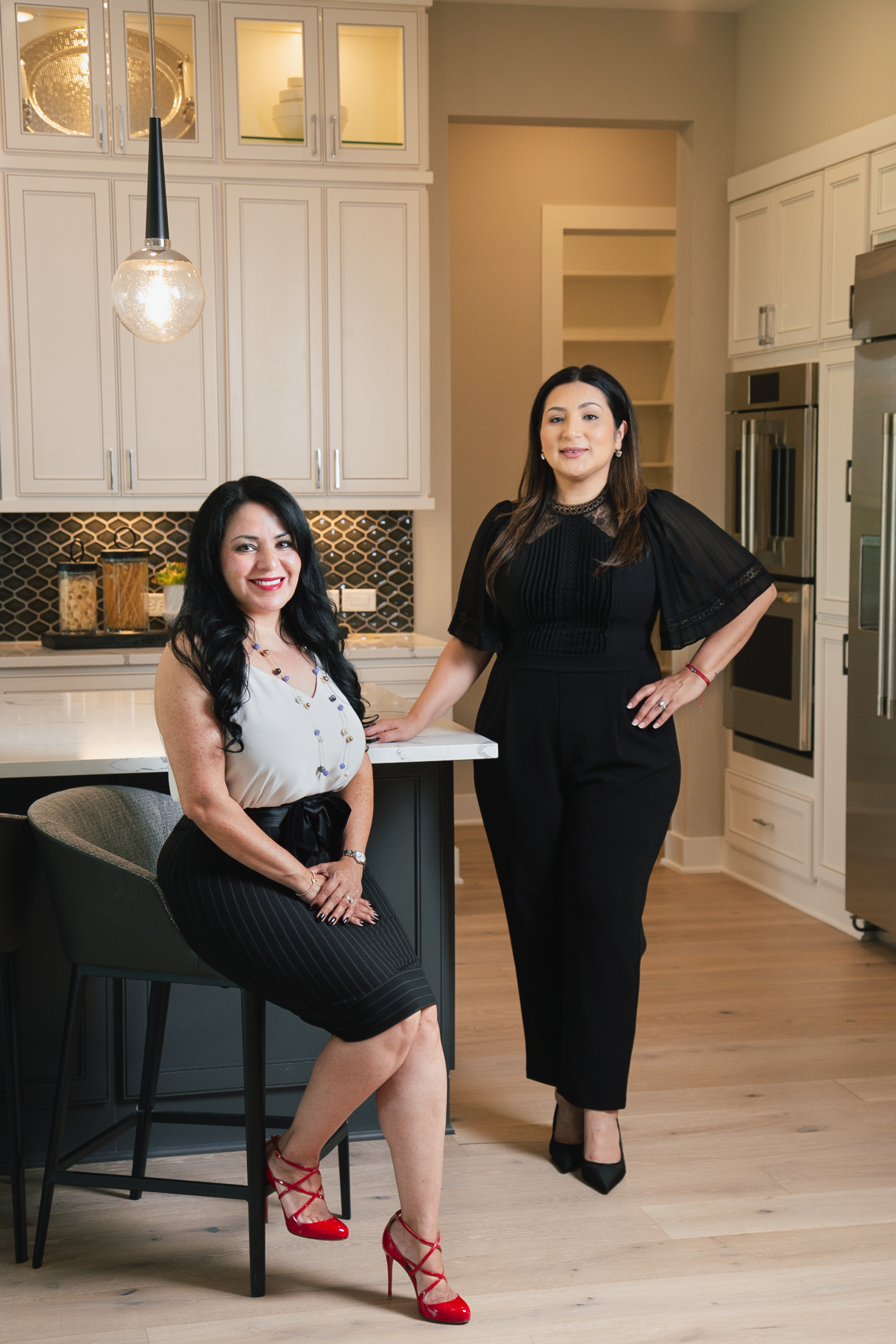 Two women in a modern kitchen, one seated on a stool and one standing by the counter.