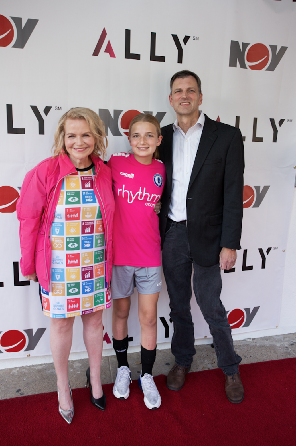 Three people stand in front of an Ally-branded step-and-repeat backdrop on a red carpet.