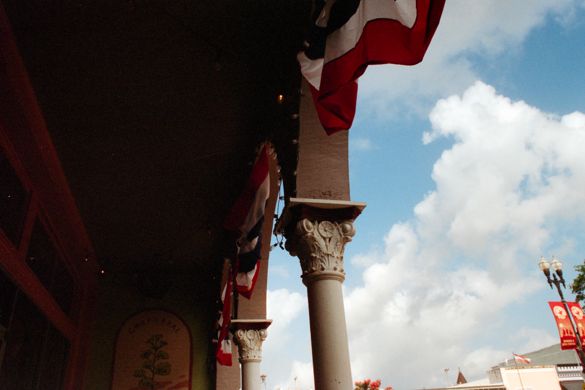 A building with a covered porch featuring ornate columns and red, white, and blue banners against a sunny blue sky.