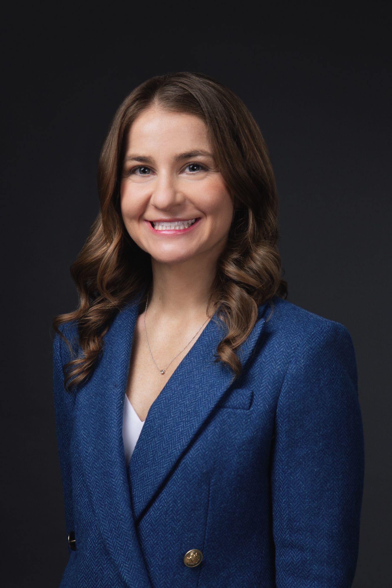 Executive headshot photograph of a smiling woman in a blue blazer against a dark studio background by Madison Avery Studio.