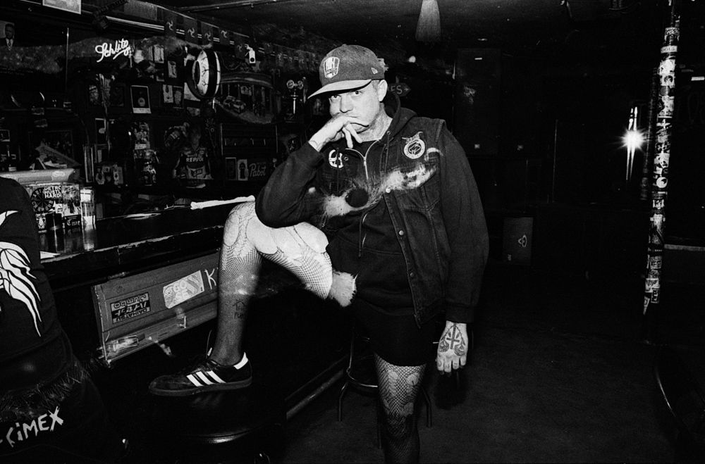 Black-and-white scene of a person leaning on a bar, hand to face, in a dimly lit nightclub interior. Shot on medium format film by Madison Avery Somerville. Developed and printed in a traditional wet darkroom by the photographer.