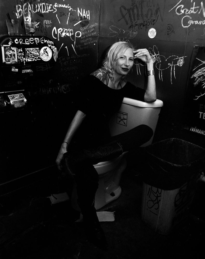 Black-and-white portrait of a person leaning in a graffiti-covered restroom, resting on a sink. Shot on medium format film by Madison Avery Somerville. Developed and printed in a traditional wet darkroom by the photographer.
