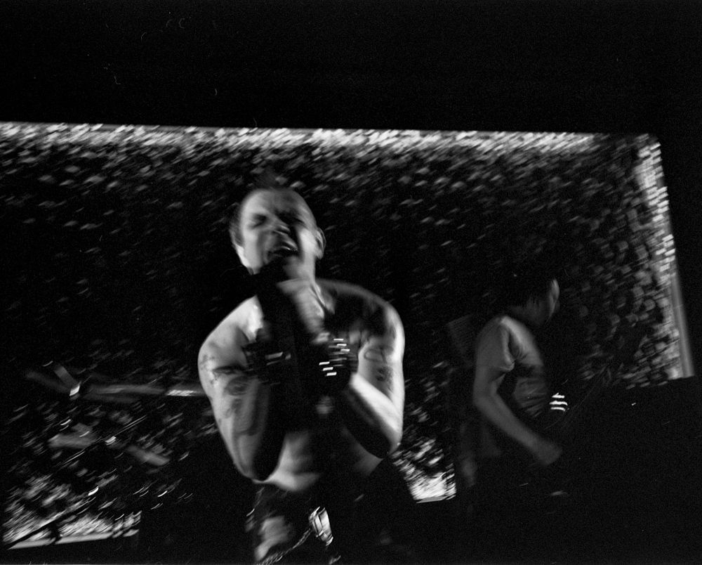 Singer performing onstage in black-and-white, holding a microphone with another musician in the background. Shot on medium format film by Madison Avery Somerville. Developed and printed in a traditional wet darkroom by the photographer.