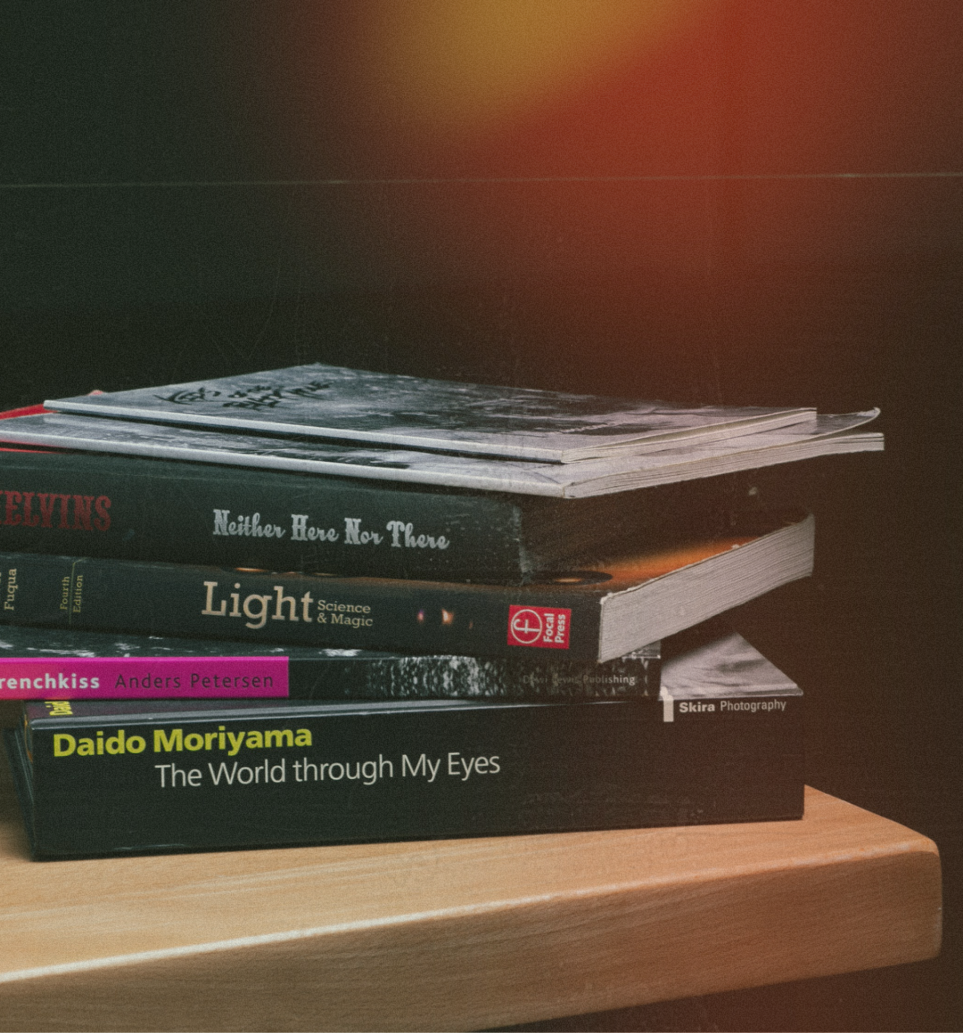 Stack of photography books on a wooden table against a dark background.