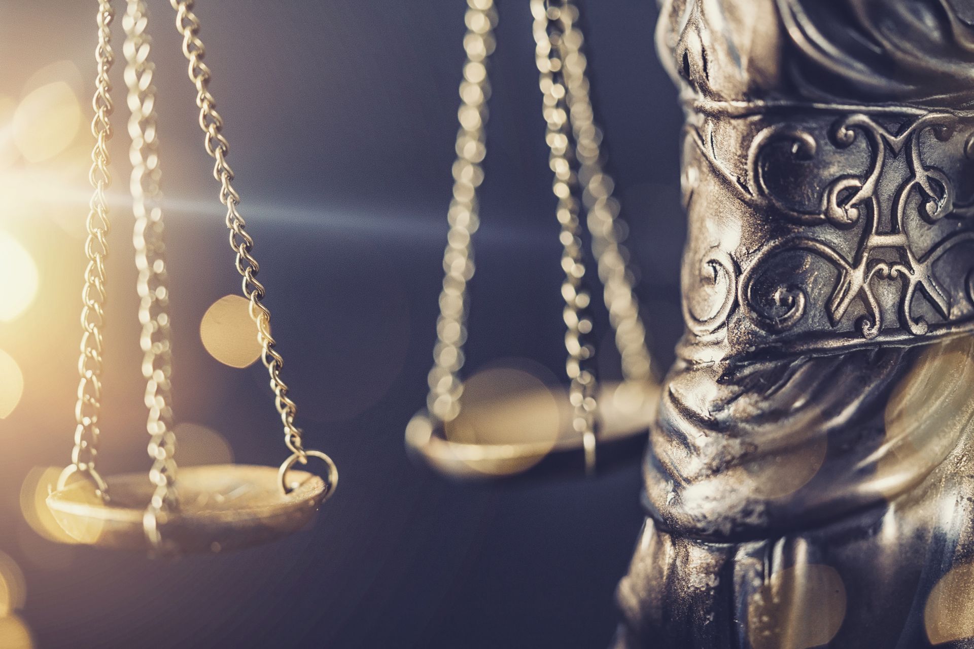 Close-up of a statue of Lady Justice, featuring scales and draped garment, with blurred background.