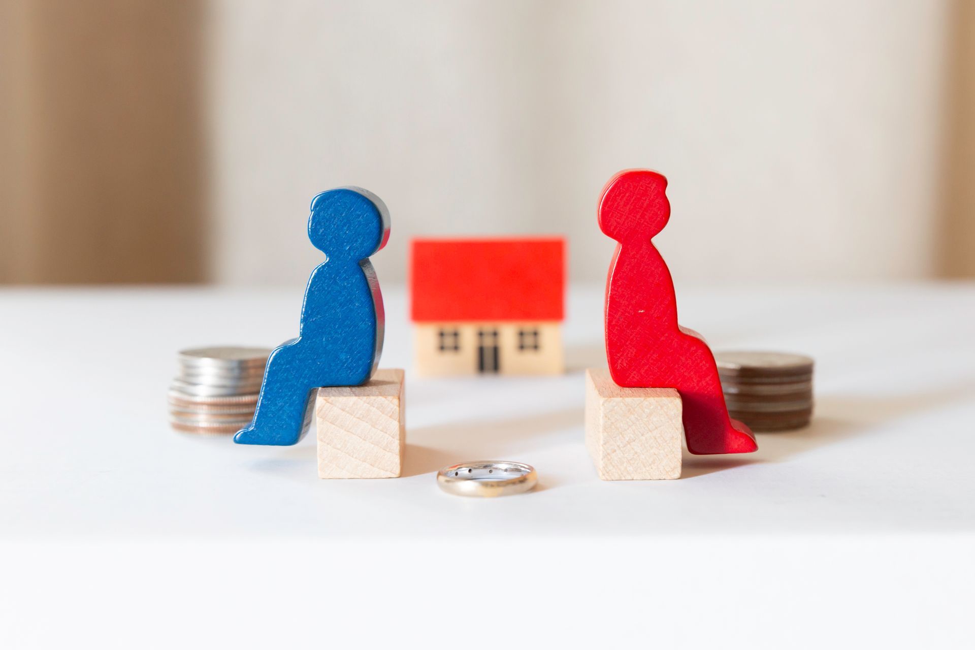 Two figures, blue and red, sit across from each other, representing a house and coins, signifying a division of assets. Two figures, blue and red, sit across from each other, representing a house and coins, signifying a division of assets.