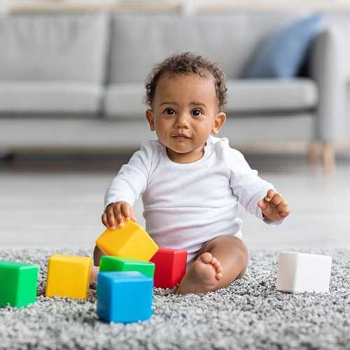 Baby sitting on a rug with colorful toy blocks in a living room