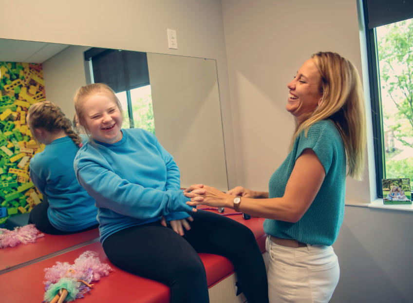 A pediatric provider is examining a  girl on a medical exam table. They are both laughing.