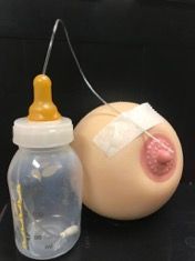 Transparent bottle with a wire attached to a taped skin-colored ball and pink protrusion on a black background
