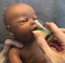 Baby doll being fed from a small glass bottle by a hand