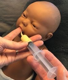 Hand feeding a baby doll with a syringe-style bottle end