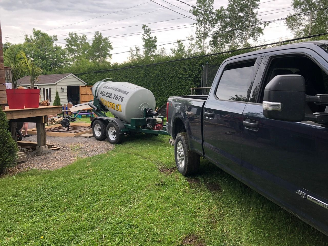 Une camionnette bleu foncé tirant une remorque malaxeur à béton sur une pelouse herbeuse devant une cour arrière.