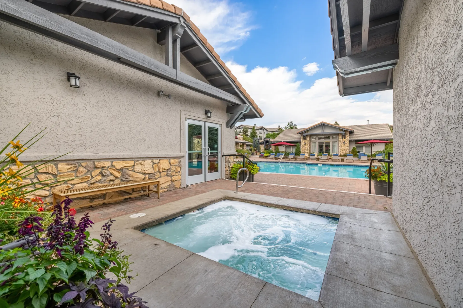 Outdoor community pool and hot tub with lounge chairs and a building in the background at Montrachet apartments in Lakewood, CO.
