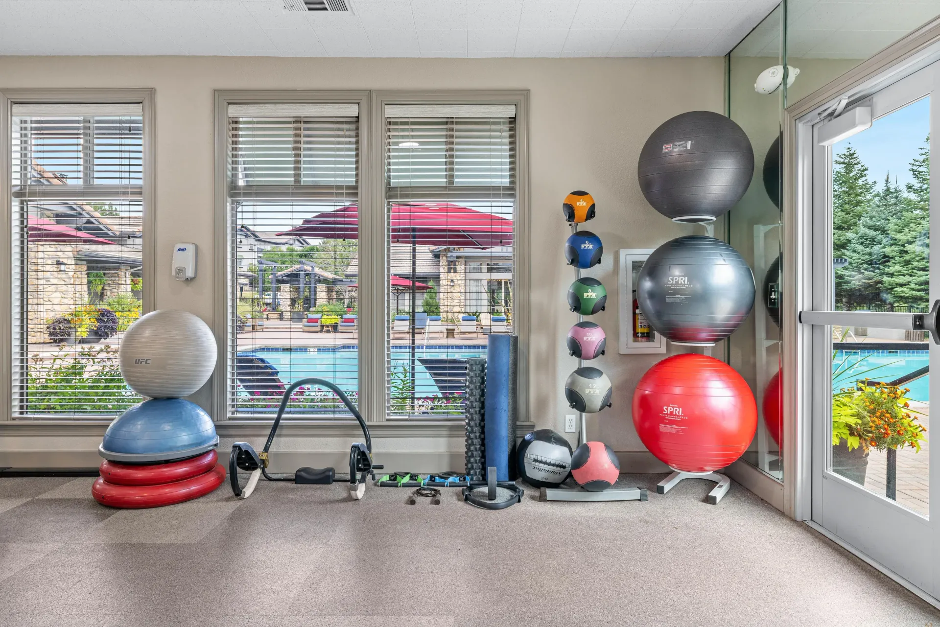 Fitness room with medicine balls, stability balls, and mats by large windows overlooking the pool at Montrachet apartments in Lakewood, CO.