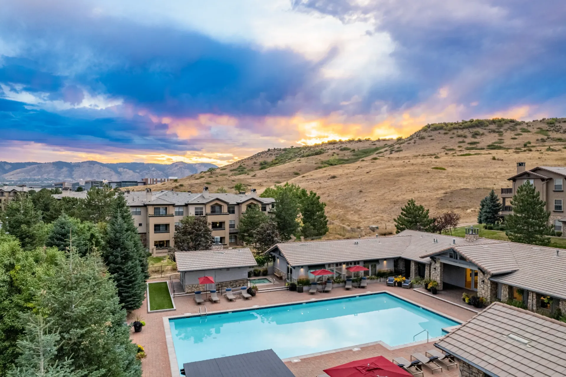Aerial view of an apartment community pool with lounge chairs, surrounding buildings, and a hillside at Montrachet apartments in Lakewood, CO.