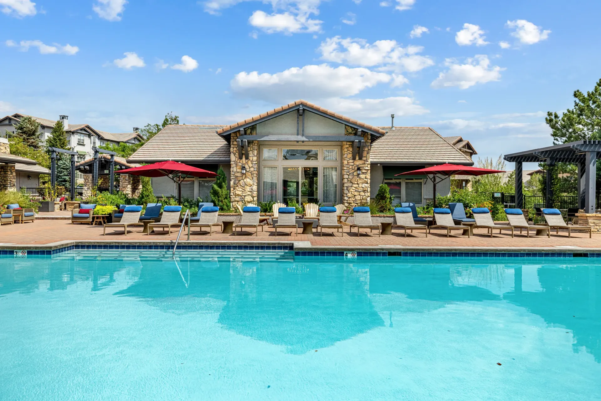 Outdoor pool with lounge chairs and red umbrellas by a clubhouse at Montrachet apartments in Lakewood, CO.