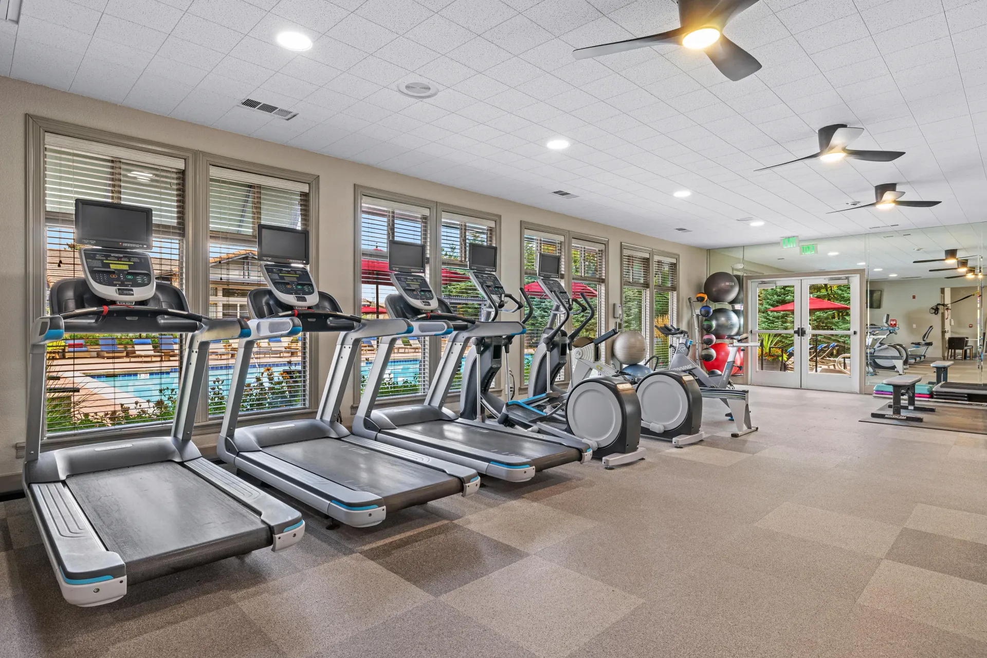 Indoor apartment gym with treadmills and cardio machines; windows overlook the outdoor pool at Montrachet apartments in Lakewood, CO.