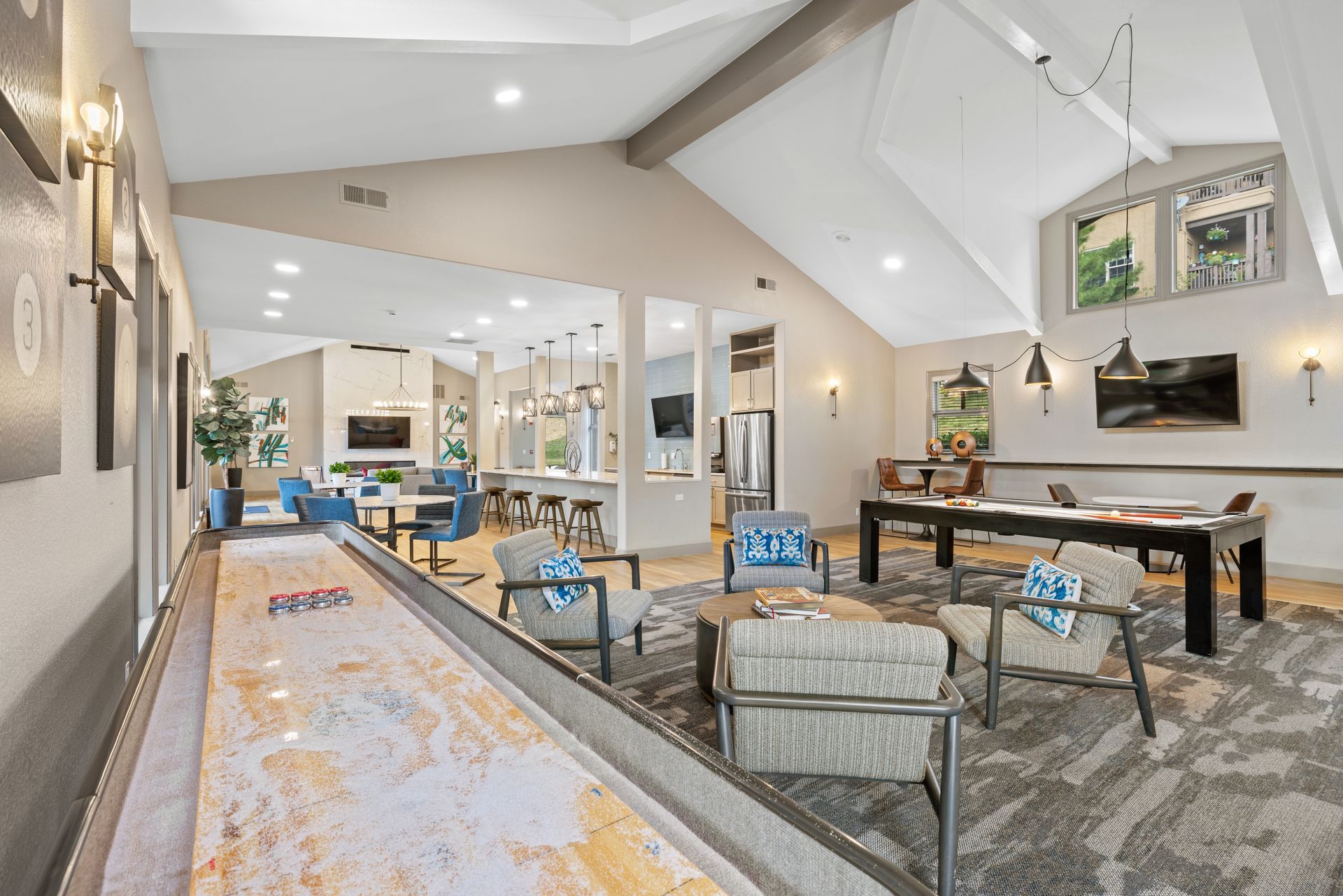 Lounge area with shuffleboard, seating, and open kitchen. Neutral tones, high ceiling, and natural light at Montrachet apartments in Lakewood, CO.